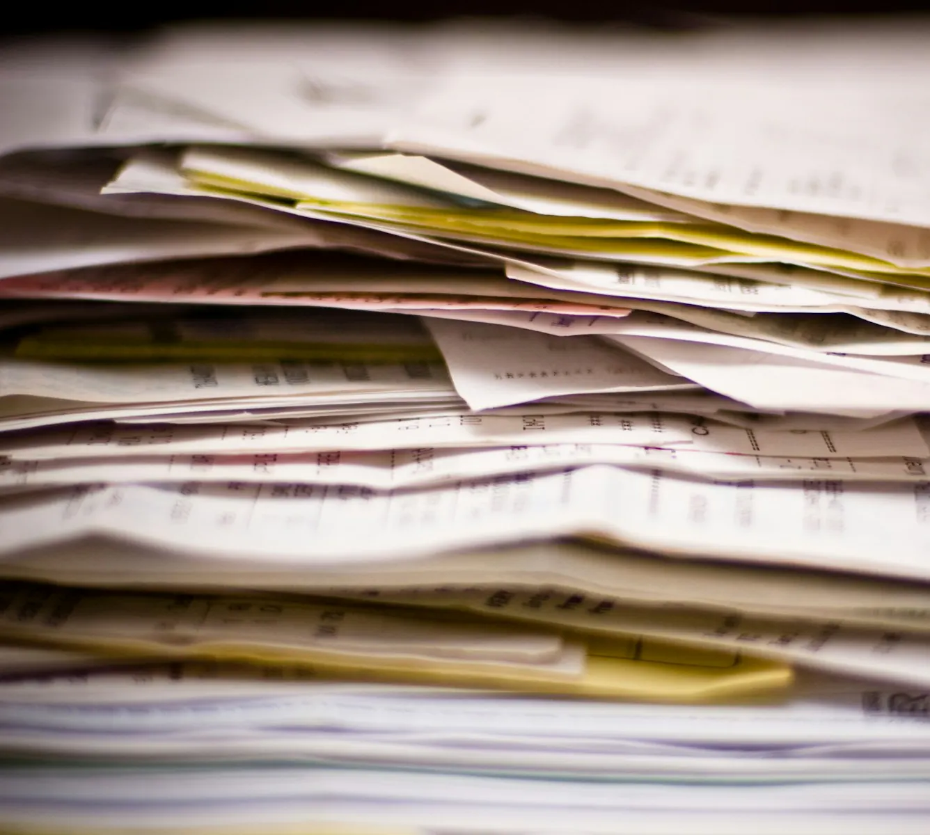 A thick stack of loose paper bills and receipts piled on a desk