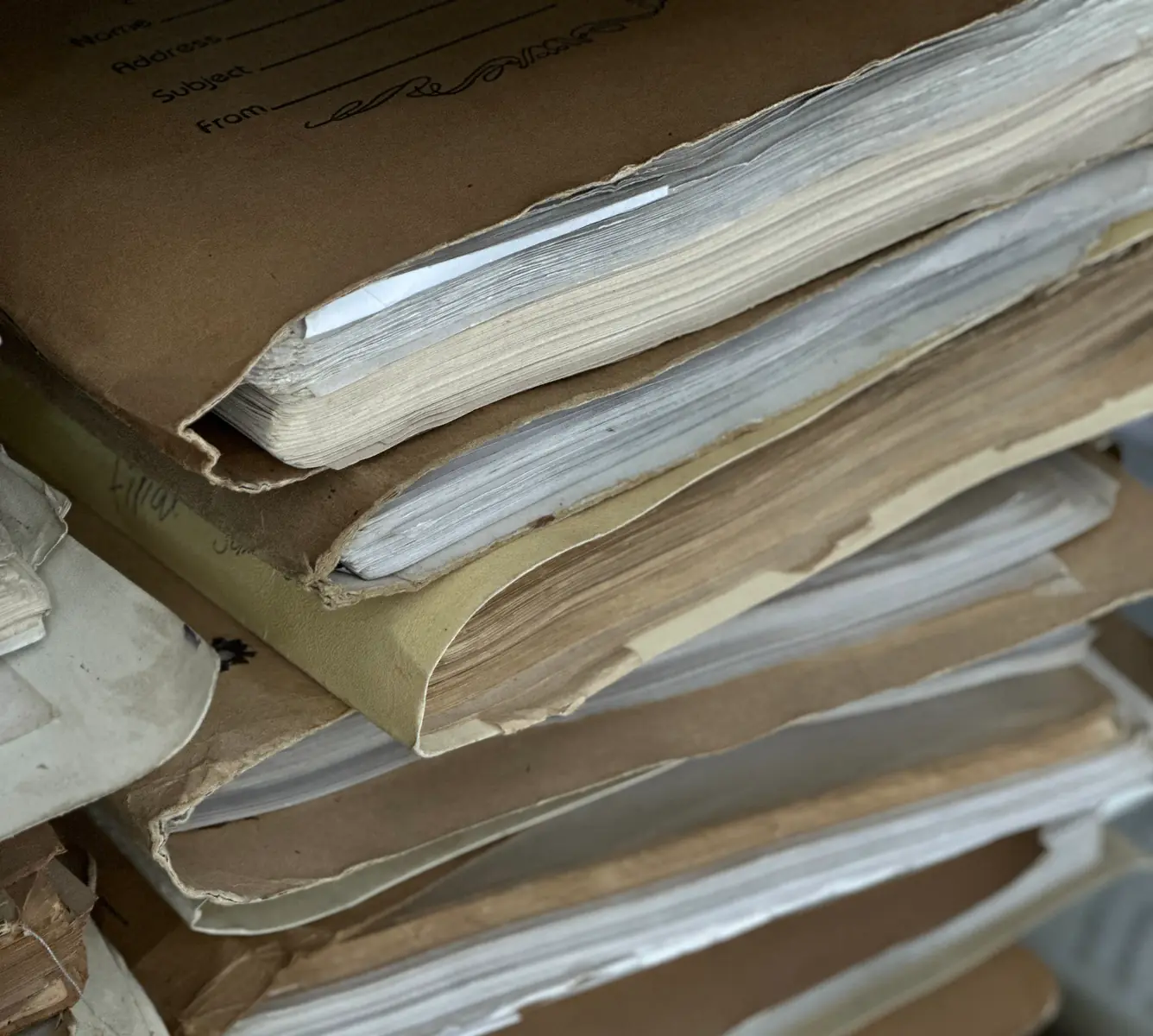 A tall stack of overstuffed paper record files, the top one printed with blank Name, Address and Subject lines